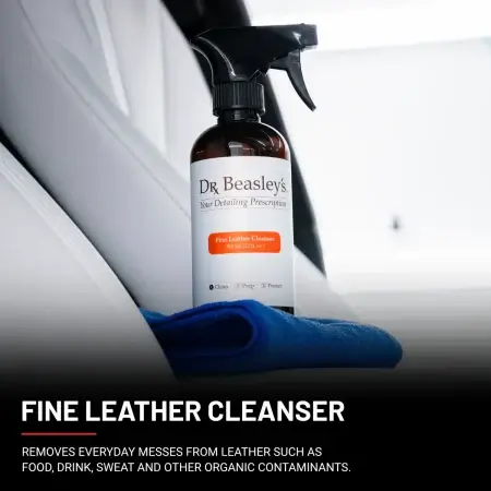 A 12 fl oz bottle of Fine Leather Cleanser positioned on the central console inside a car with white leather interior.