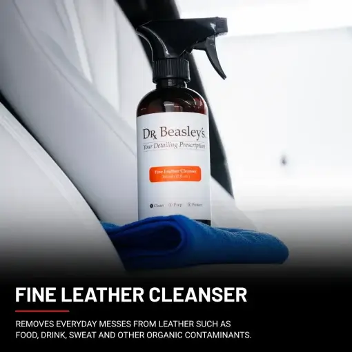 A 12 fl oz bottle of Fine Leather Cleanser positioned on the central console inside a car with white leather interior.
