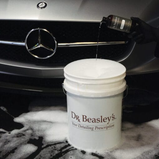 Bottle of Matte body wash being poured into bucket, in front of Mercedes