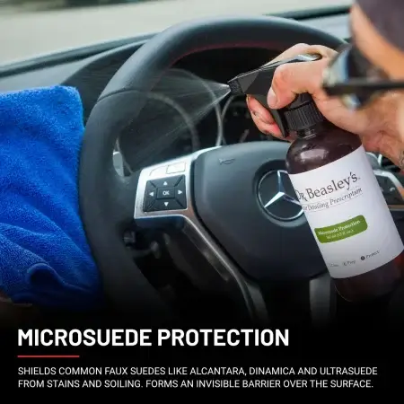Microsuede Protection 12 fl oz bottle spraying onto an Alcantara steering wheel and a blue microfiber towel.