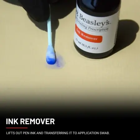 A hand wearing a black glove lifting out an ink stain using a swab dabbed into Ink Remover.