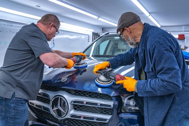 Mercedes hood being paint corrected by two detailers.