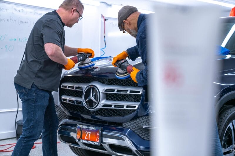 Mercedes hood being paint corrected by two detailers.