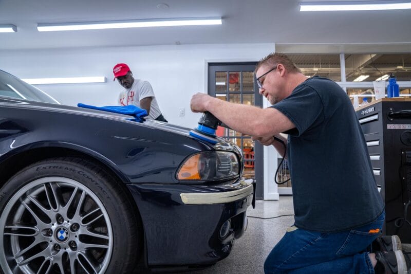 Hood of E39 M5 being paint corrected by two detailers.