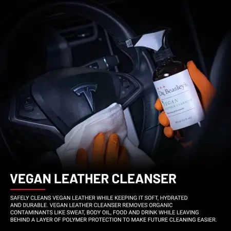 A man wearing orange gloves wipes a black vegan leather Tesla steering wheel with a microfiber towel after spraying Vegan Leather Cleanser.