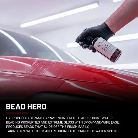 A hand wearing a black glove sprays Bead Hero onto the glossy red hood of a car.
