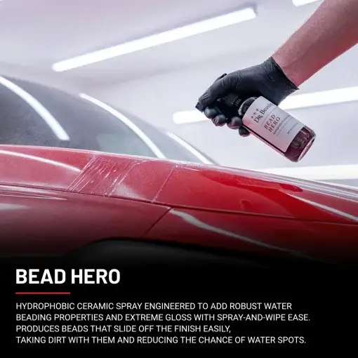 A hand wearing a black glove sprays Bead Hero onto the glossy red hood of a car.