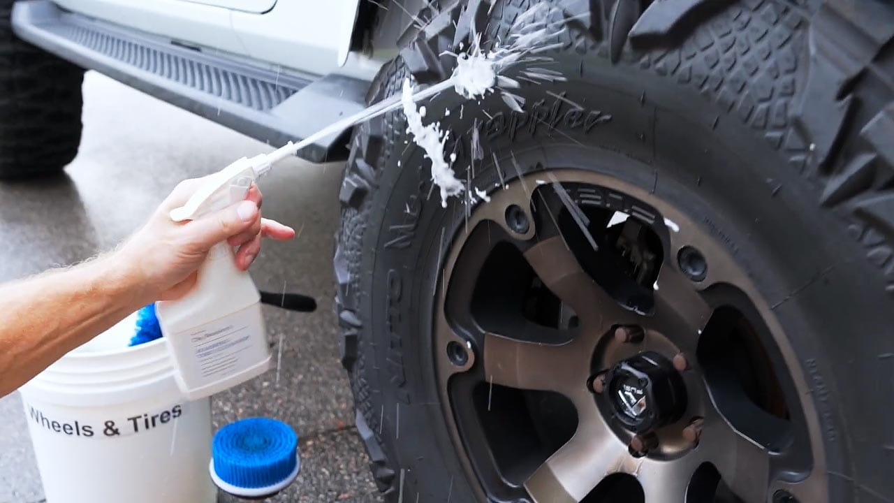 Tire cleaning solution being sprayed onto a car wheel during the cleaning process, showing foam application for removing dirt, brake dust, and road grime