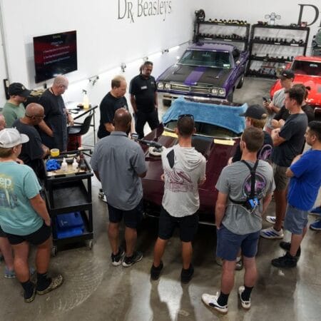 Mike Phillips leads a detailing lesson with students gathered around a burgundy Corvette in the training shop.