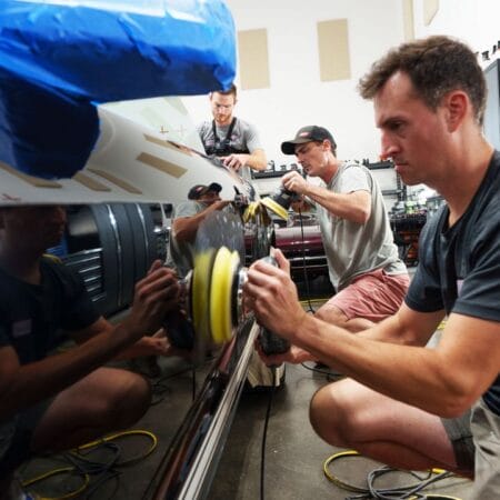 Students practice machine polishing the side panels of a black Ford Mustang during hands-on detailing training.