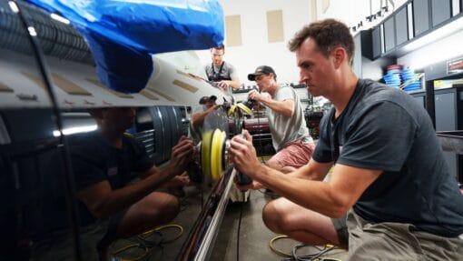 Students practice machine polishing the side panels of a black Ford Mustang during hands-on detailing training.