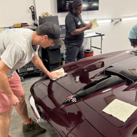 A student applies a coating to the hood of a burgundy Corvette during Mike Phillips’ detailing class.
