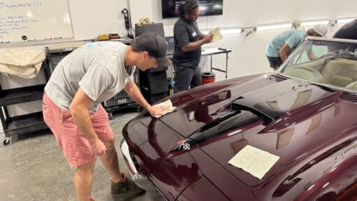A student applies a coating to the hood of a burgundy Corvette during Mike Phillips’ detailing class.