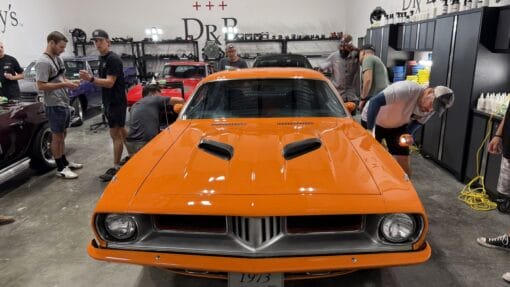Students inspect the glossy paint on an orange Plymouth Cuda using a handheld inspection light.