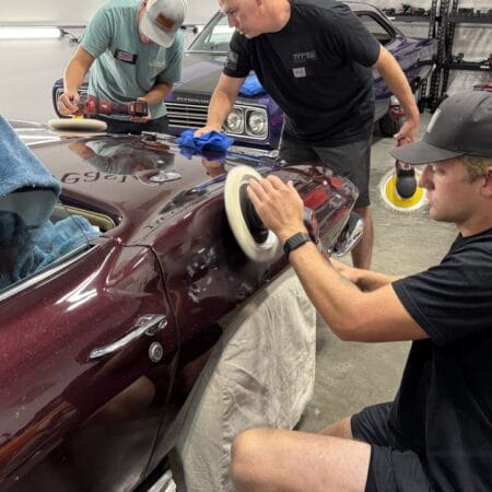 A student machine polishes the curved rear quarter panel of a burgundy Corvette during hands-on detailing training.