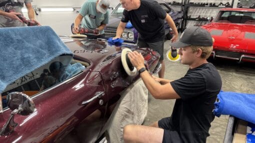 A student machine polishes the curved rear quarter panel of a burgundy Corvette during hands-on detailing training.