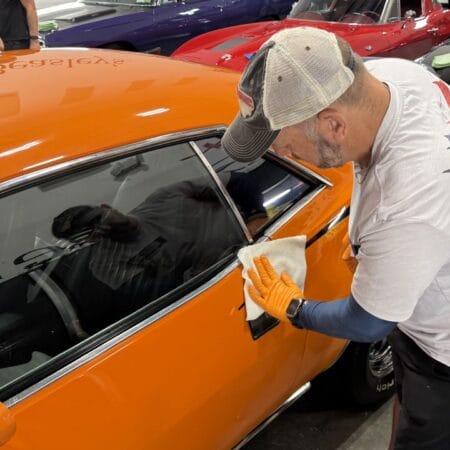 Students wearing gloves apply coating to the side panels of an orange Plymouth Cuda.