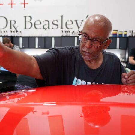 A student uses a handheld inspection light to check the red paint on a Corvette during detailing class.