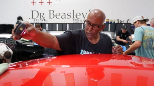 A student uses a handheld inspection light to check the red paint on a Corvette during detailing class.