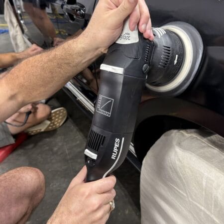Close-up of a student using a RUPES machine polisher on the rear quarter panel of a black Ford Mustang.