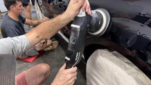 Close-up of a student using a RUPES machine polisher on the rear quarter panel of a black Ford Mustang.