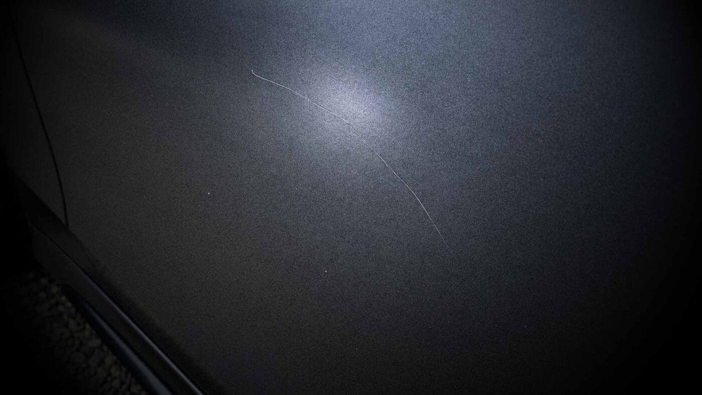 A scratch on matte car paint after the matte finish has been cleaned.