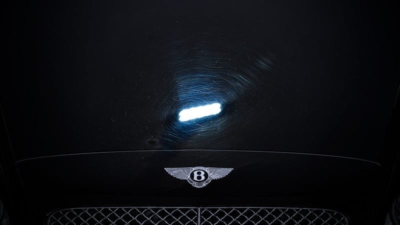 Inspecting car paint scratches under a detailing light before polishing
